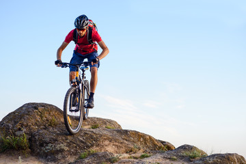 Cyclist in Red Riding the Bike Down the Rock on the Blue Sky Background. Extreme Sport and Enduro Biking Concept.