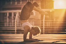 Young Woman Practicing Yoga, Standing In Vrischikasana Scorpion Pose In The Terrace At Sunset