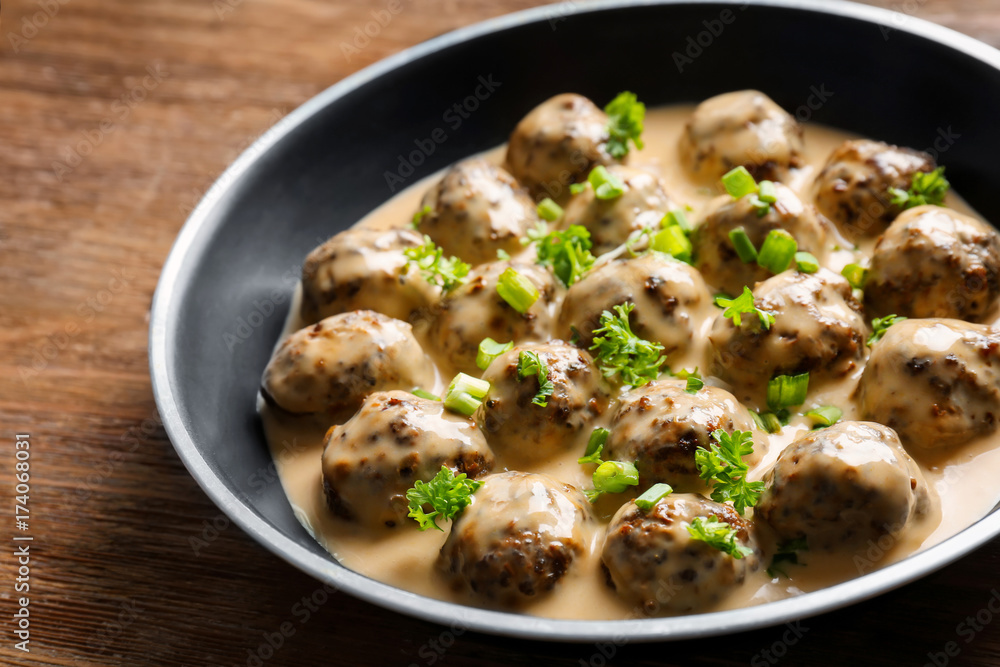 Frying pan with delicious meatballs in sauce on wooden table