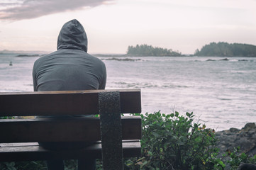 Sad and lonely man sitting on bench overlooking sea on Vancouver Island