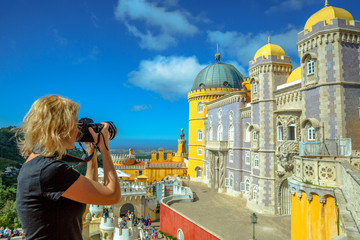 Travel woman photographer takes photos of Pena National Palace. Female photographer with professional camera takes shot of the most visited attraction in Sintra, Portugal. Travel and tourism in Europe