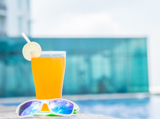 Wall Mural - Sunglasses with orange juice and a piece of lemon at the side of swimming pool. Vacation, beach, summer travel concept