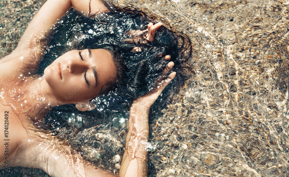 beautiful young woman lying down in water on the beach - obrazy, fototapety, plakaty 