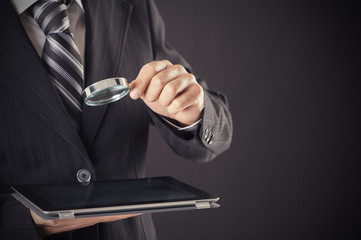 Businessman holding magnifying glass and digital tablet concept