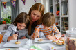 © lordn - Mother and children glazing cookies for Halloween celebration
