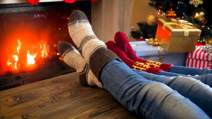 Family in wool socks relaxing by the fireplace at room decorated for Christmas