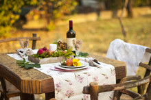 Romantic Feast. Autumn Picnic. Yellow Leaves. Garden. Ceramic Tableware. Flowers And Fruits. Garnet. Textile. Wine At Sunset