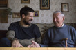 © Jovana Milanko/Stocksy - Grandpa and his adult grandson sitting at the table talking