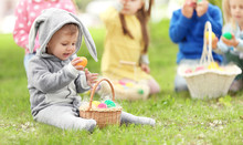 Cute Little Boy With Basket On Green Grass In Park. Easter Egg Hunt Concept