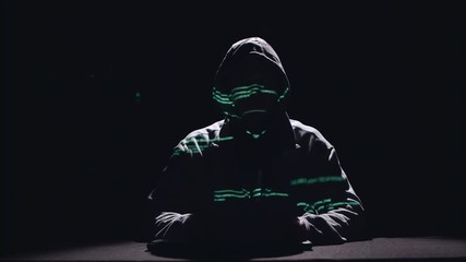 Spy is typing virus patches on the keyboard for hacking. Black background. Silhouette