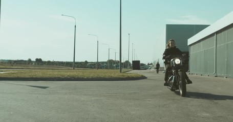 Wall Mural - TRACKING Beautiful Caucasian female biker riding her motorcycle near warehouse. 4K UHD RAW edited footage