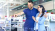 © Gorodenkoff - In the Electronics Store Beautiful Young Couple are Looking for New Electrical Device. Men Points his Finger at Something. Store is Big, Bright and Has all the New Devices.