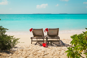 Wall Mural - Christmas on beach -chair lounges with Santa hats at sea