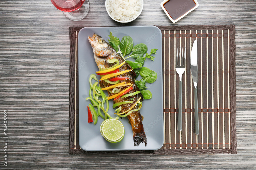 Serving plate with delicious fish in sauce and garnish on table