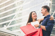 © Nusara - Couple man and woman hug girlfriend and holding red shopping bag in city outdoor on building background