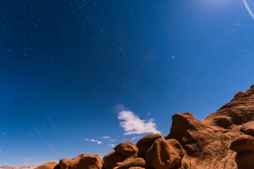 Night sky with full moon rising, or moonrise, in Goblin Valley State Park in Utah showing clouds, stars, and canyons silhouettes in wilderness nature