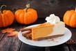 Slice of pumpkin cheesecake with whipped cream on a dark rustic wood background