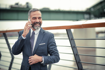 Smart senior business man, an elderly entrepreneur and business owner, talking over his cell phone in an outdoors urban area