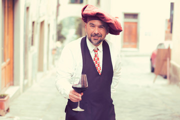 Portrait of a mature happy man with glass of red wine outdoors in old italian village