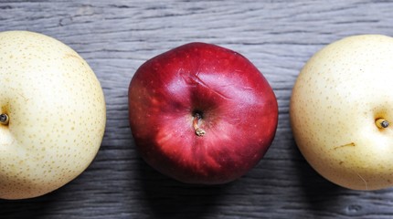 raw organic of 2 yellow Asian apple pears and 1 red apple in the middle on wooden table background