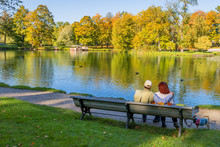 Happy Couple Of Seniors Are Resting On The Wooden, City Public Park, The Early Autumn In Europe