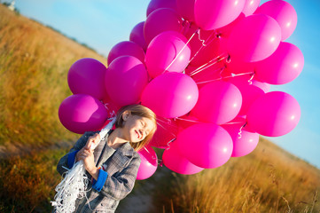 Happy toddler birthday girl in autumn field holding many pink balloons,smiling and laughing ready to celebrate holiday