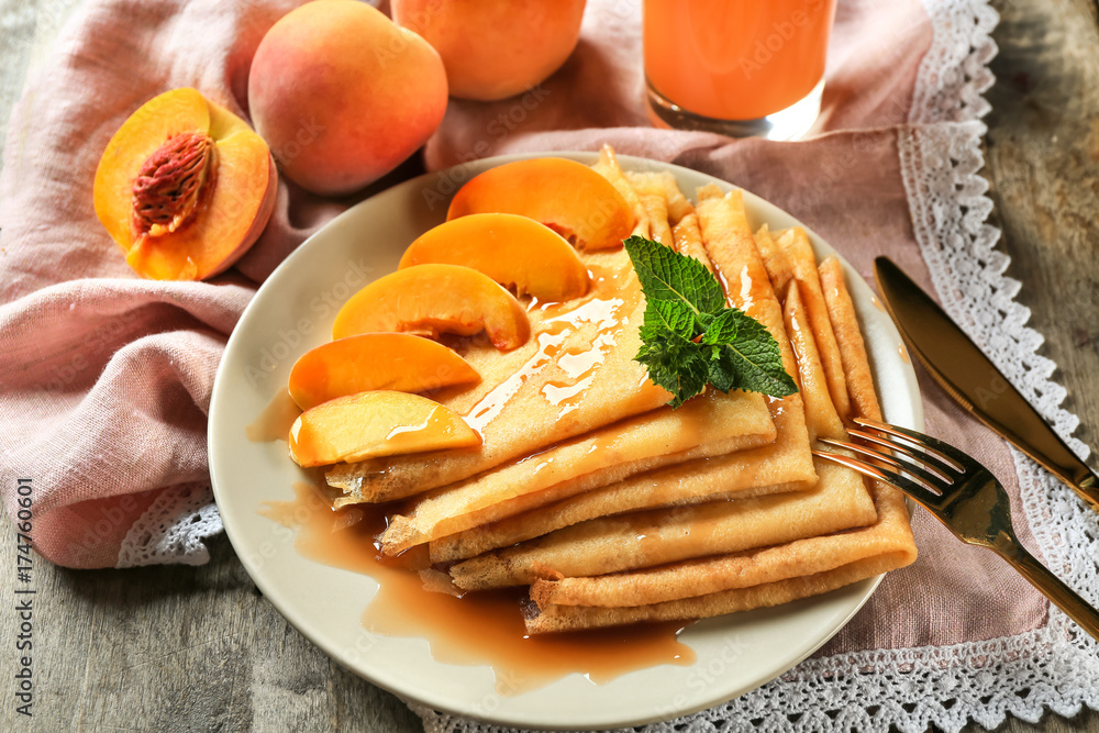 Plate with tasty thin pancakes and peaches on table