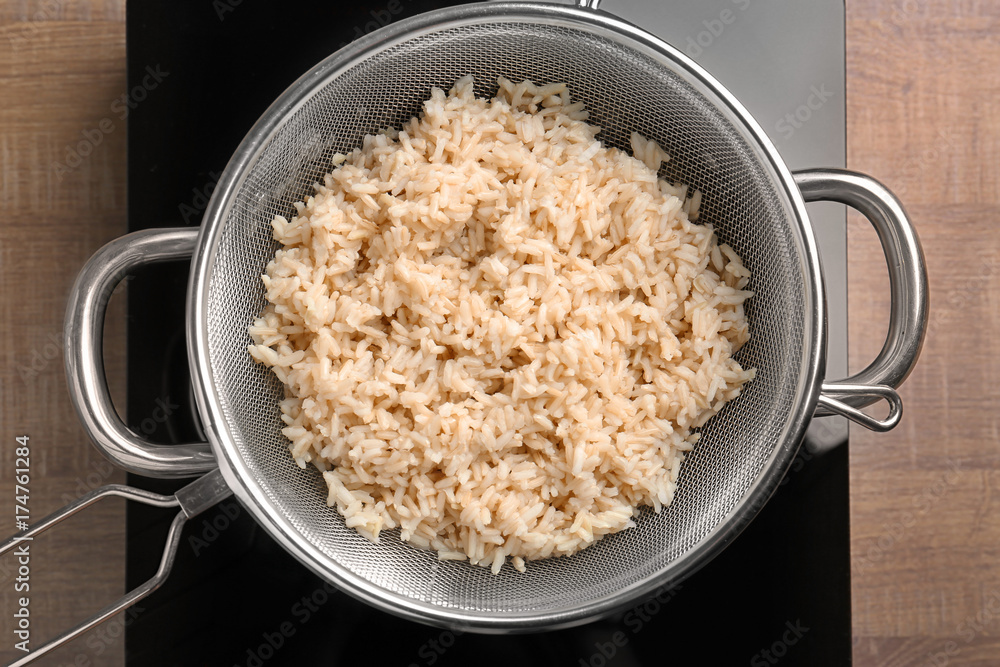 Sieve with brown rice in saucepan on stove