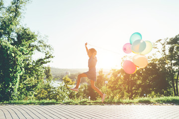 Cute girl holding colorful balloons in the city park, playing, r