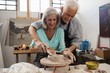 Senior man assisting senior woman in making pottery during