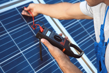 Young worker checking installation of solar panels by using multimeter