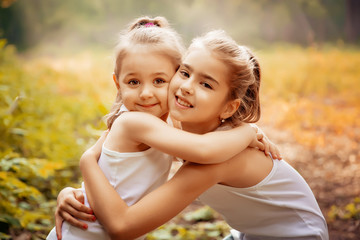 childhood, family, friendship and people concept - two happy kids sisters hugging outdoors.