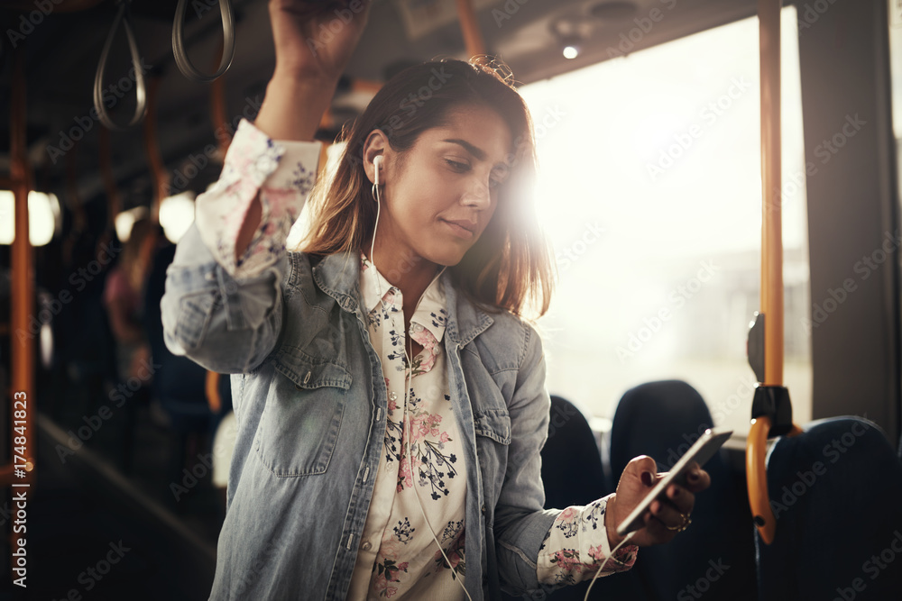 Young woman standing on a bus listening to music - obrazy, fototapety, plakaty 