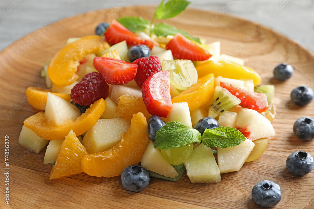 Delicious fruit salad on wooden plate, closeup