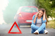 © Africa Studio - Upset young woman with cell phone sitting on road near broken car