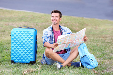 Young man with map sitting on green grass outdoors