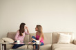 © fizkes - Two young girlfriends sitting on sofa at home and having personal conversation. Girls relax and chat about different topics. Best friends have cup of coffee, female friendship. Copy space for text.