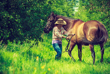 Western Woman Walking On Green Meadow With Horse