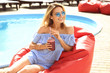 © Africa Studio - Beautiful young woman with fresh smoothie sitting on bean bag chair near swimming pool