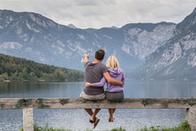 Embraced Casual Couple Watching Tranquil Overcast Morning Scene At Lake Bohinj, Alps Mountains, Slovenia.