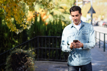 Wall Mural - Young man in urban background listening to music with headphones