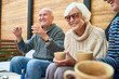 © Seventyfour - Cheerful senior friends gathered together at cozy small patio and remembering funny stories from their past, they wearing knitted sweaters and warming themselves with herbal tea
