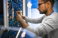 Young Man Connecting Cables In Server Room