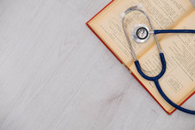 Beautiful Stethoscope Lying On A Reference Books. Stethoscope With Open Book On Wooden Background. Medical Literature Concept. Copy Space For Text, Selective Focus Top View