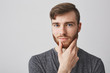 © Cookie Studio - Close up portrait of good-looking caucasian man with ginger beard and brown hair touching beard with hand,looking in camera with calm expression.