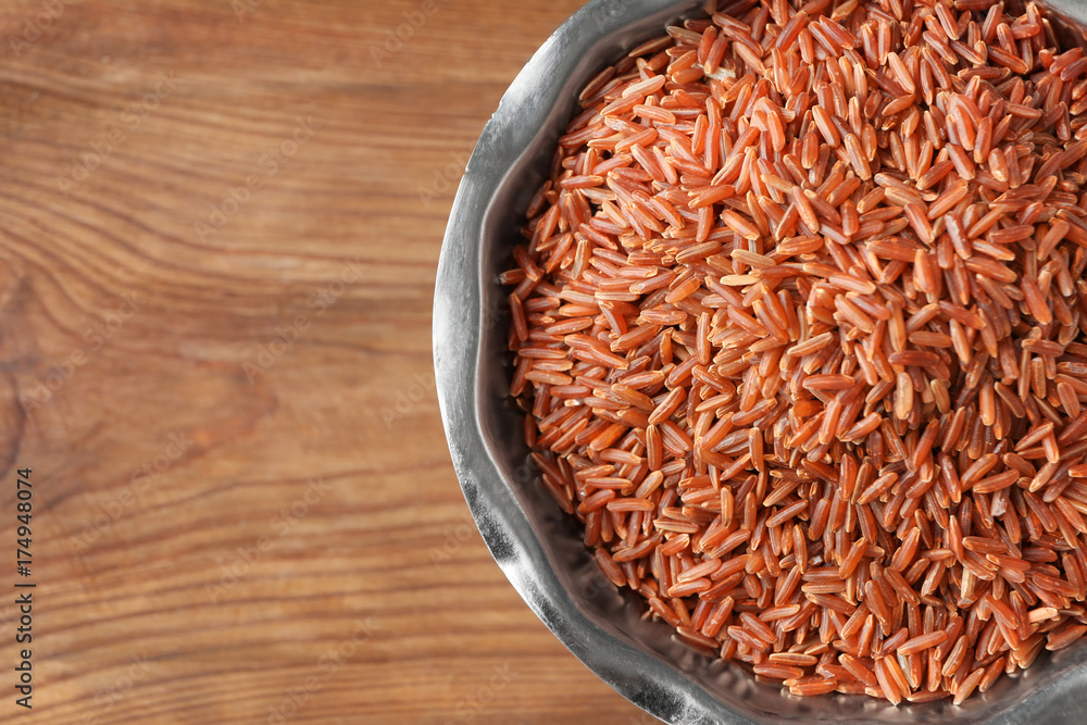 Bowl with raw red Cargo rice on wooden background