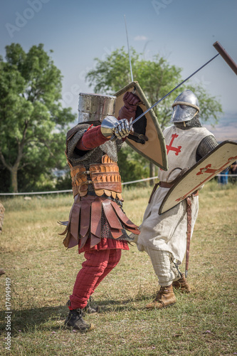 Fotografía Medieval knight battle with swords and shields, reenactment with costumed characters and medieval armor with chainmail, helmet swords and shields