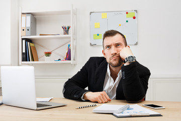 Young bored businessman with laptop in modern white office