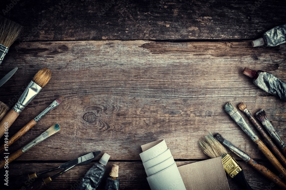 Paint tubes, brushes for painting and palette knifes on old wooden background. Top view. Flat lay. Retro toned. - obrazy, fototapety, plakaty 