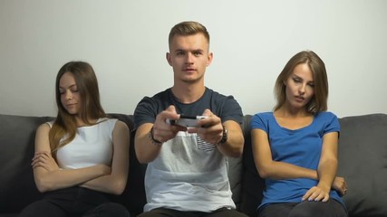 Wall Mural - Cute caucasian teen girls tired of gripped teen boy playing a video game on the comfortabe sofa, slow motion